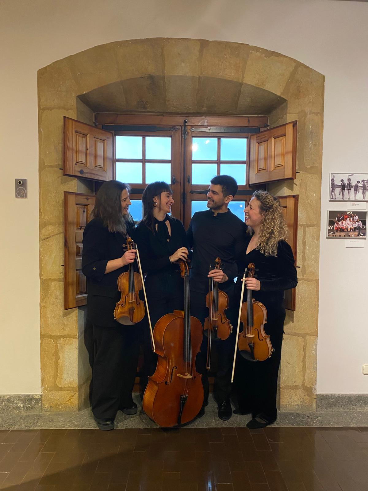 Los cuatro integrantes de Aralar Quartet compartiendo sonrisas con sus instrumentos junto a una ventana